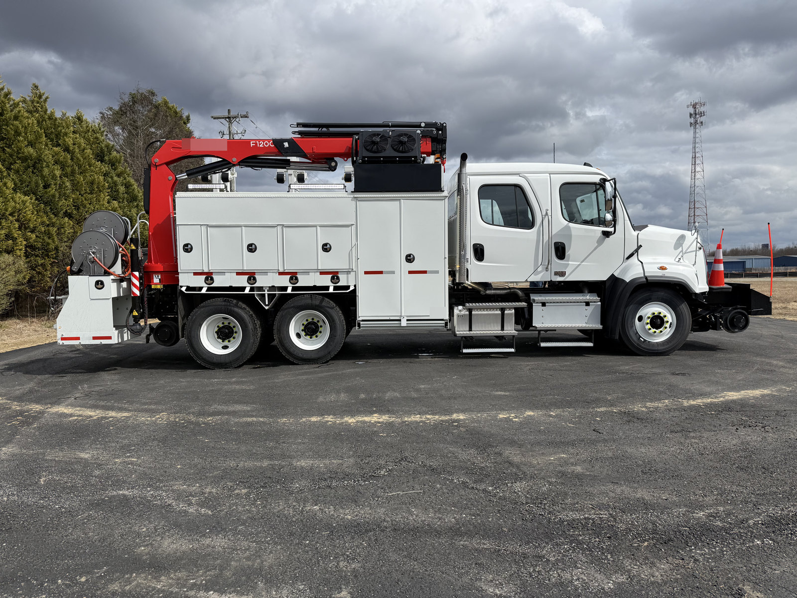 Side view of a white equipment truck with a folded red crane and hose reels outdoors