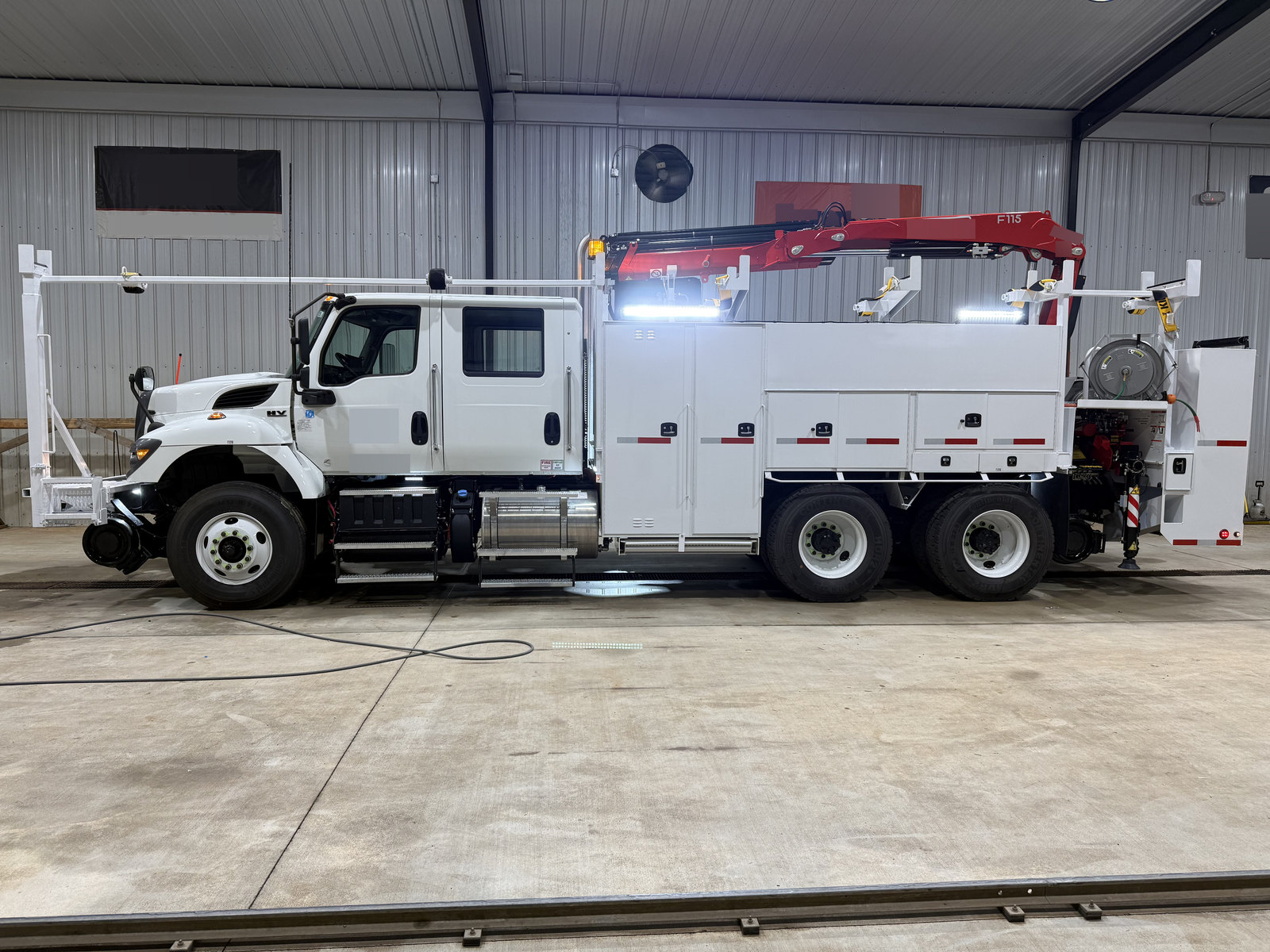 Side view of a white equipment truck with a folded red crane inside the workshop